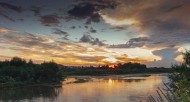 Ön planda, nehir, arka planda, bulutlardaki gökyüzü, gün batımında.