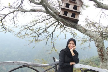 Güvercin kafesinin altında poz veren Asyalı bir kadının portresi. Hafta sonları tepede tatilin tadını çıkar..