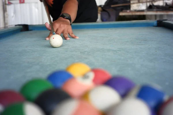 men\'s hands playing billiards on a blue carpeted table. a portrait of a professional player with a blurry billiard ball foreground. the first step of the billiard game begins