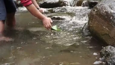 Bir adam temiz bir nehirde bambu yapraklarından yapılmış bir tekneyi oynuyor. Endonezya 'daki kırsal çocuklar için basit bir oyun. Ormanın ortasında suyla oynayarak doğanın güzelliğinin tadını çıkar.