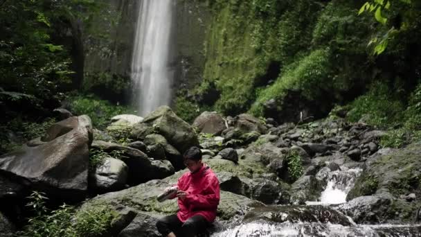 Портрет Азиата Красной Куртке Наслаждающегося Свежестью Водопада Посреди Леса Человек — стоковое видео