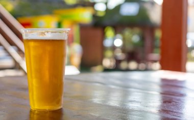 Plastik bardakta bira kahverengi bir masanın üstünde bulanık bir arka planı var.