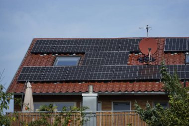 Wohnhaus Dach belegt mit Solarpanelen. Das Haus steht im vollen Sonnenschein hinter einem grossen Apfelbaum mit rot leuchtenden pfeln. Auf dem grossen Balkon steht ein zugeklappter Sonnenschirm. Ein Sinnbild of Solarenergie und bewusstes Leben