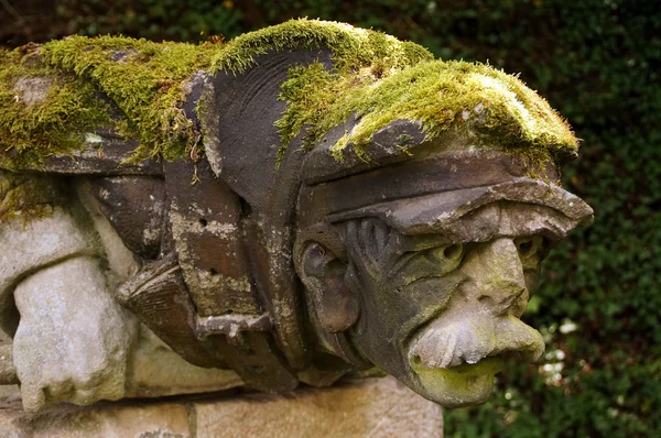 Gargoyles in the form of an old man - the cap and the back overgrown with moss. — Stock Photo, Image