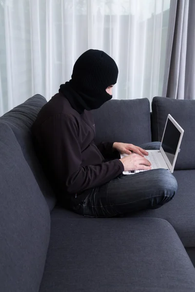 Criminal at home hacking with his laptop — Stock Photo, Image