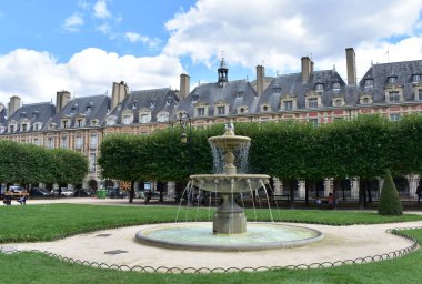 Paris, France. August 14, 2019. Fountain at Place des Vosges, the oldest square in the city located at Le Marais district, with people taking a break and having fun.