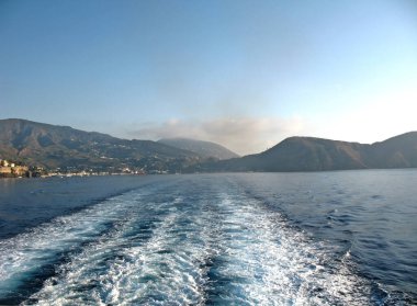 Geminin arkasında bir iz ve filmin ortasında Etna volkanından duman. Solda, Sicilya kıyılarında, Milazzo kasabasında..