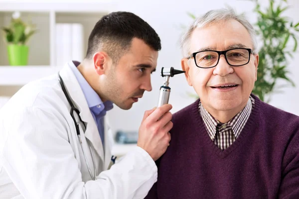Dokter memegang otoskop dan memeriksa telinga pasien — Stok Foto