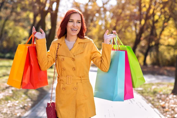 Mujer feliz en abrigo amarillo sosteniendo bolsas de compras — Foto de Stock