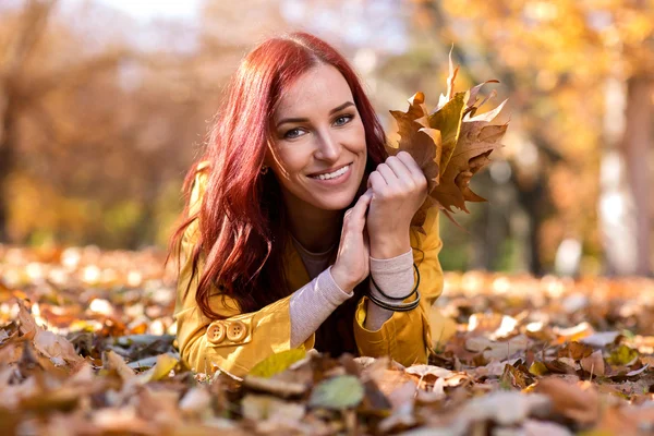 Menina sorridente deitado em folhas de outono — Fotografia de Stock