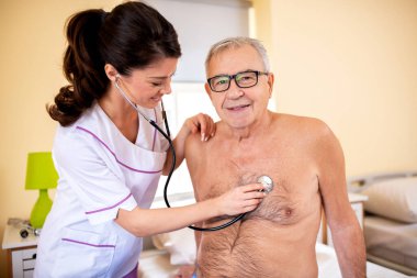 Genç esmer doktor, yaşlıları kontrol etmek için steteskop kullanıyor. Huzurevi konsepti.