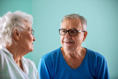 Yaşlı bir adam ve yaşlı bir kadın bir huzurevinde yatağında oturmuş sohbet ediyorlar.