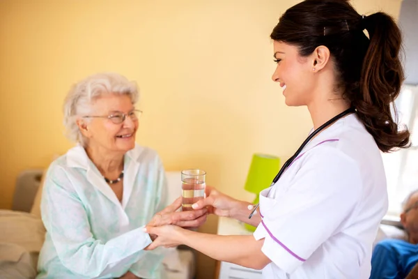 Lady doctor handing a glass of water to elder woman nursing home occupant, providing care to elders concept