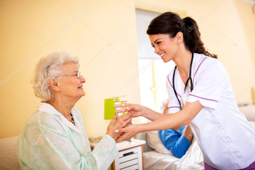 Caring young female doctor bringing glass of water to her patient in a nursing facility