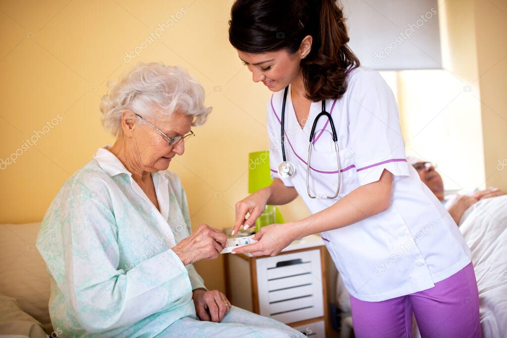 Brunette lady doctor and her nursing home elder woman patient having polite conversation, skilled nursing facility concept