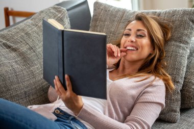 Kanepede uzanmış kitap okuyan genç bir kadın yaşam tarzı konsepti okuyor.