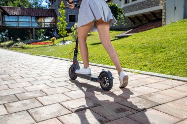 Patikalı yolda elektrikli scooter kullanan genç bir kadın, bacak şutu konsepti