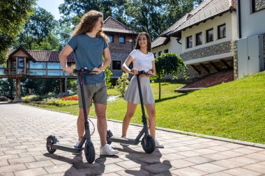 Genç bir adam ve genç bir kadın yeni scooterlarını denerken dışarıda eğleniyorlar.