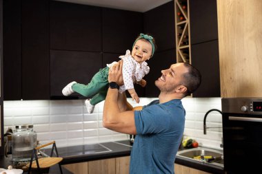 Gururlu genç baba, küçük kızını kollarında tutuyor ve eğleniyorlar.