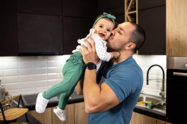 Mutlu genç adam, kızını kollarına alıp onunla oynarken onu öpüyor.