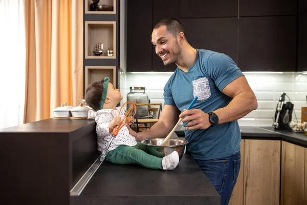 Proud young dad teaching his infant child about preparing food in the kitchen of the apartment, dad baby daughter concept