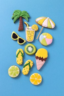 Tropik yaz plaj içeceği süslemeli kurabiyeler, palmiye ağacı, güneşlik, plaj topu, terlikler, dondurma, narenciye, mavi arka plan konsepti.