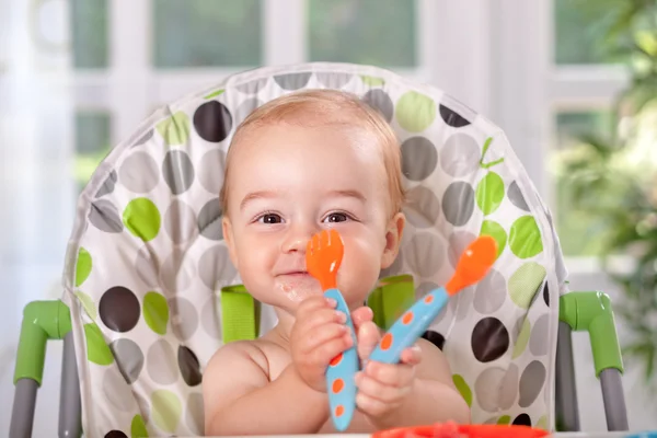 Smiling beautiful baby eating with spoon and fork — Stock Photo, Image