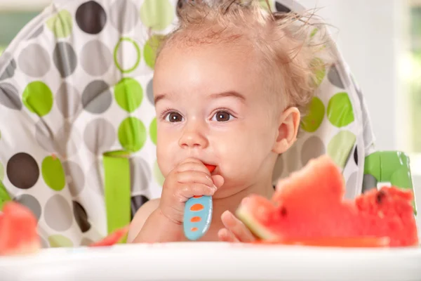 Ragged bebê segurando colher em si e comer melancia — Fotografia de Stock