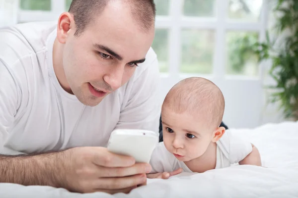 Padre y bebé niño usando teléfono inteligente y acostado en la cama —  Fotos de Stock