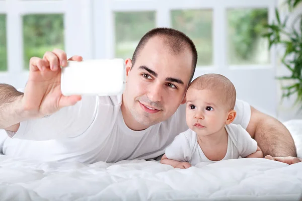 Família feliz com câmera em casa na cama — Fotografia de Stock