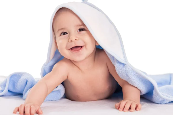 Smiling baby lying on bed under towel — Stock Photo, Image