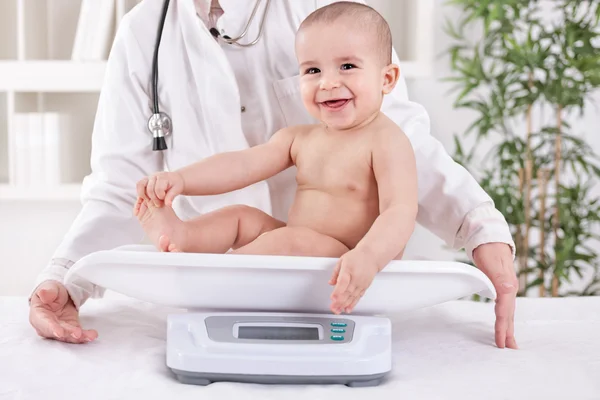 快乐微笑的婴儿在 pedrician 的办公室，测量体重 图库照片