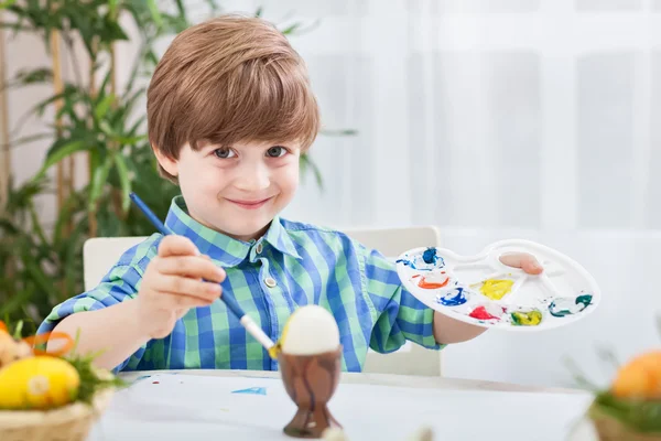 Vakkert smilende barn maler egg, lager børste og holder colo – stockfoto