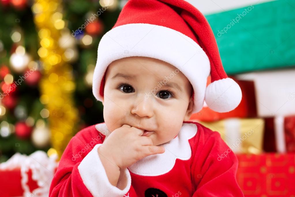 Cute baby santa claus with fingers in mouth
