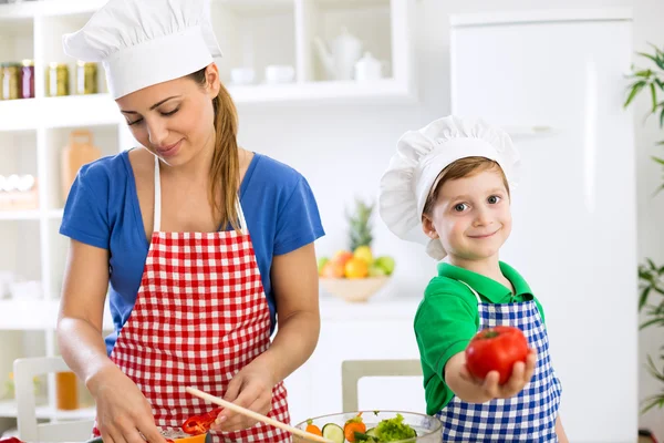 Ibu memasak makan siang dan anak kecil yang lucu memegang tomat — Stok Foto