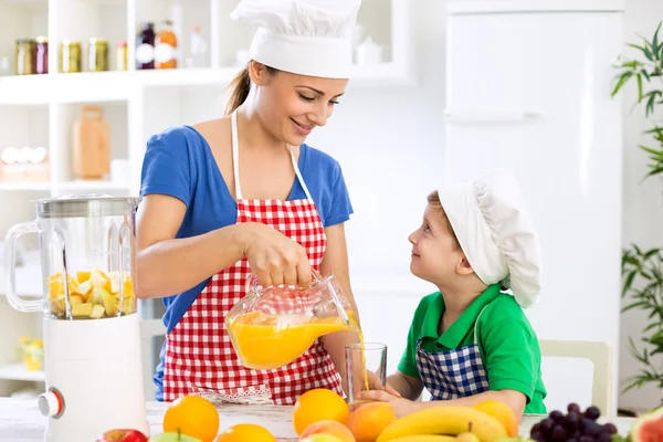美丽的快乐母亲给她孩子男孩倒橙汁 — 图库照片