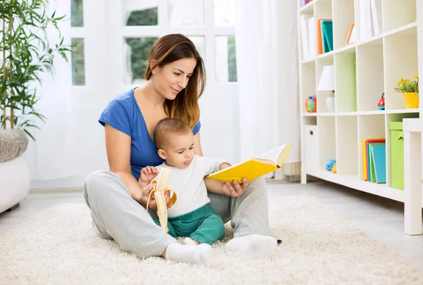 Young mother telling a story to her baby and giving banana for s — Stock Photo, Image