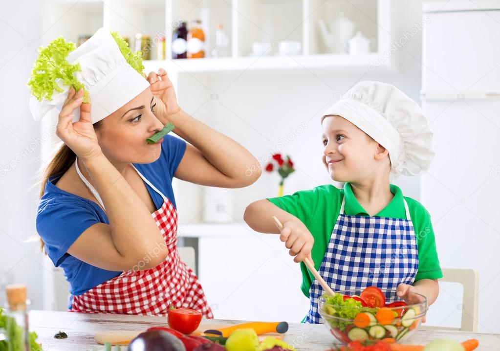 Mother and child having fun in kitchen playing with vegetables a