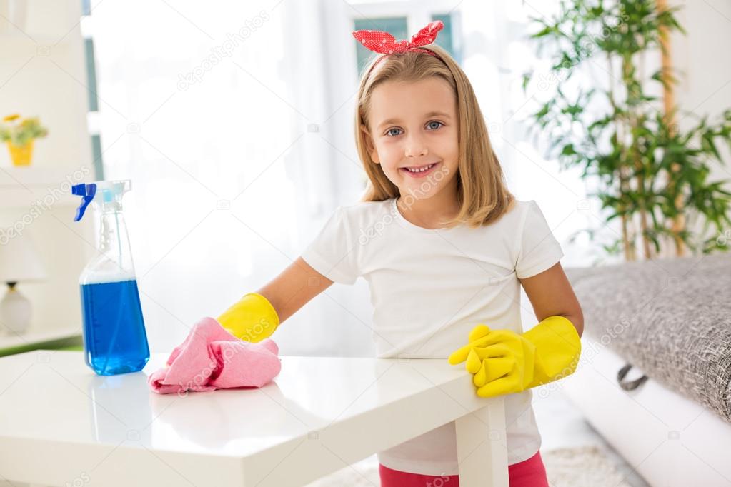 Adorable worth girl holding pom and cleaning a table at living r