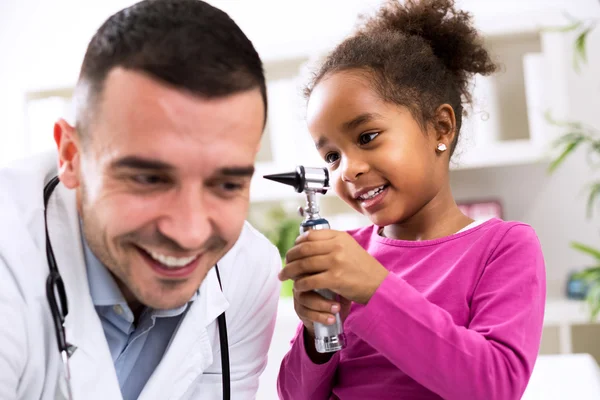 Kleines afrikanisches Mädchen hält Otoskop in der Hand und spielt mit Kinderärzten — Stockfoto