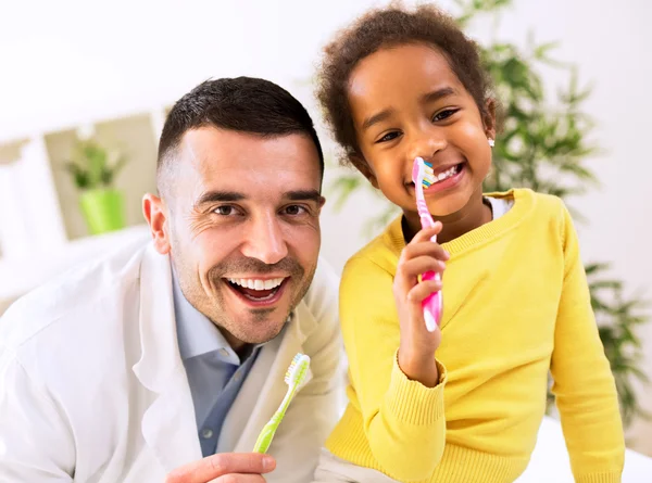 Beautiful girl and pediatrician brushing teeth together — Stock Photo, Image