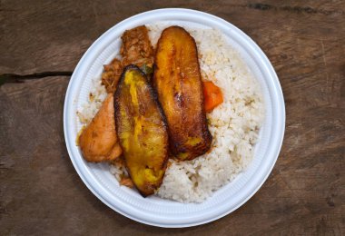 Panama için tipik yemek, muz dilimleri, tavuk, pirinç ve sebzeler, plastik tabakta servis edilen sokak satışı, ahşap arka plan, çok lezzetli yemekler.