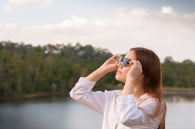 Asyalı kadının portresi güneş gözlüğü tutuyor ve ormanda dinleniyor.