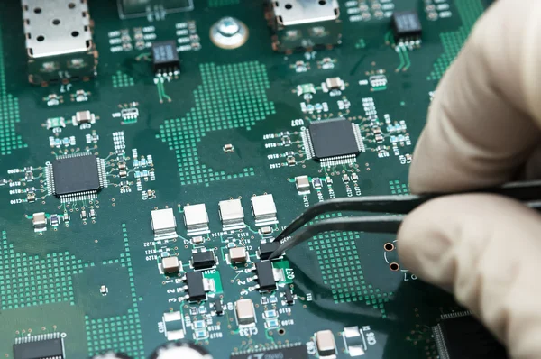 Hand with tongs on a PCB — Stock Photo, Image