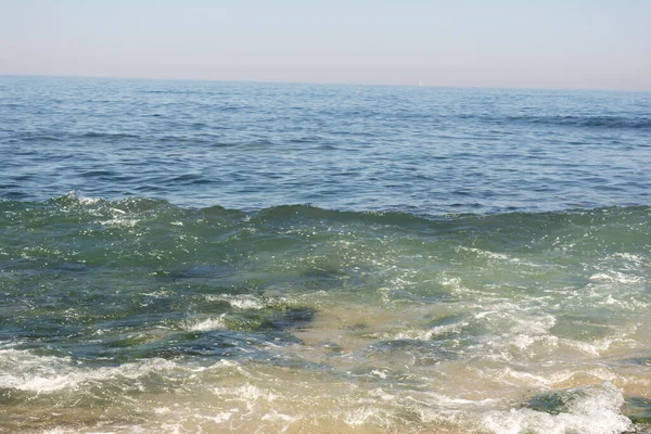 Tembel bir yaz öğleden sonrasında, mavi gökyüzüyle kumsalda yumuşak dalgalar kopar.