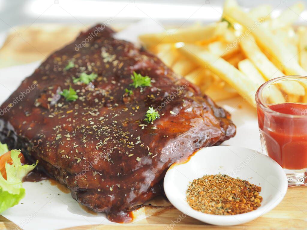 Pork Spareribs BBQ, Barbeque Pork Ribs with french fries vegetable salad, tomato sauce in a clear glass on wooden tray, food delicious