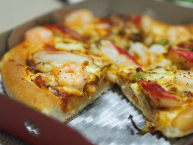 Üstünde karides, yengeç çubuğu, jambon, ananas ve sos karton kutuda.