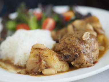 Massaman körisi. Tavuklu beyaz pirinç. Masada beyaz tabak var.