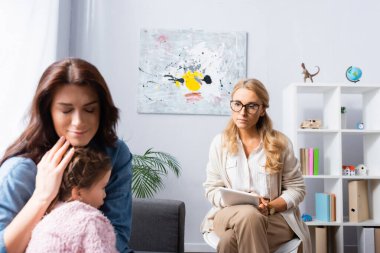 Endişeli, gözleri kapalı bir anne, psikoloğa giderken kızını kucaklıyor.