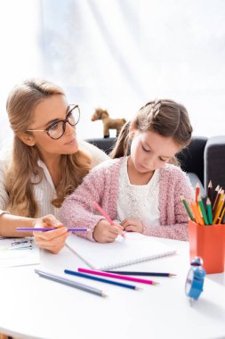 little girl drawing pictures with colorful pencils while visiting psychologist clipart